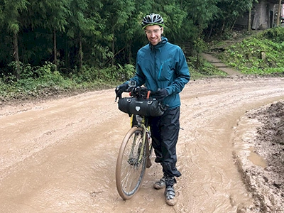 Stewart Law stood on a muddy road in China. Pictured with his Genesis Steel Frame Touring Bike.
